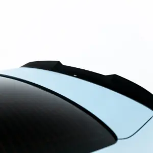 Close-up of a car roof edge showing a black rear spoiler above a tinted rear window against a pale sky.