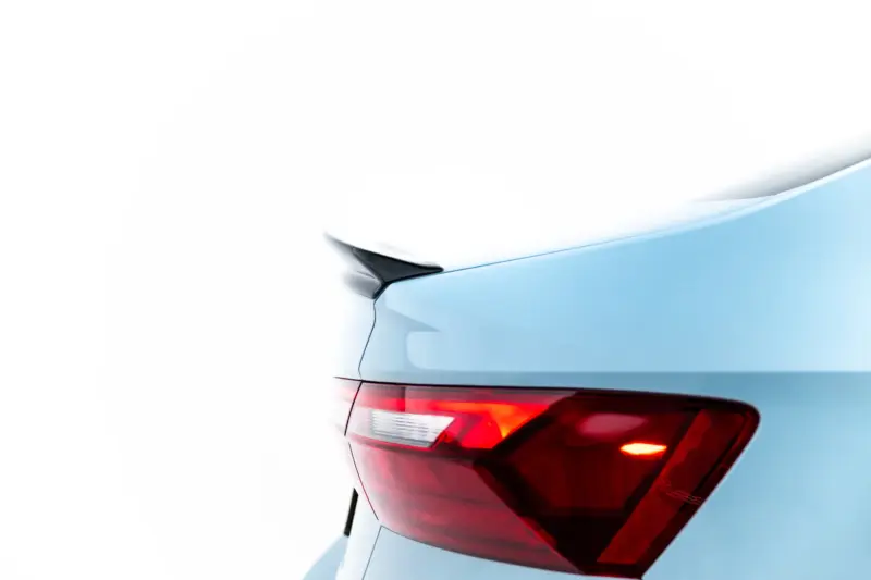 Rear left corner of a light blue car showing the tail light and trunk edge.