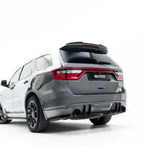 Rear three-quarter view of a gray SUV showing taillights, roof spoiler, and dual exhausts in a studio setting.