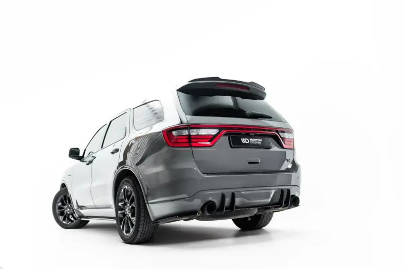 Rear three-quarter view of a gray SUV showing taillights, roof spoiler, and dual exhausts in a studio setting.