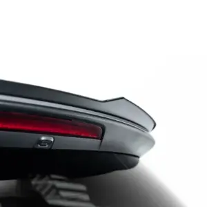 Close-up of a car's rear end showing a red taillight and the edge of the trunk against a white background.