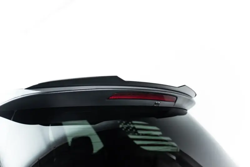 Rear view of a white car showing a black spoiler and red tail light on the hatch area.