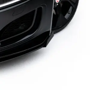 Close-up of a black car front showing the bumper, lower grille, and part of a wheel against a light background.