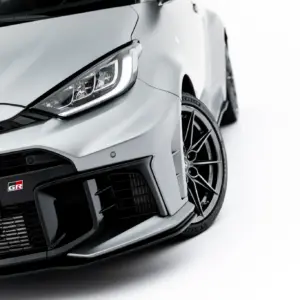 Close-up of a silver car's front-left corner, showing the headlight, bumper, and alloy wheel on a white backdrop.