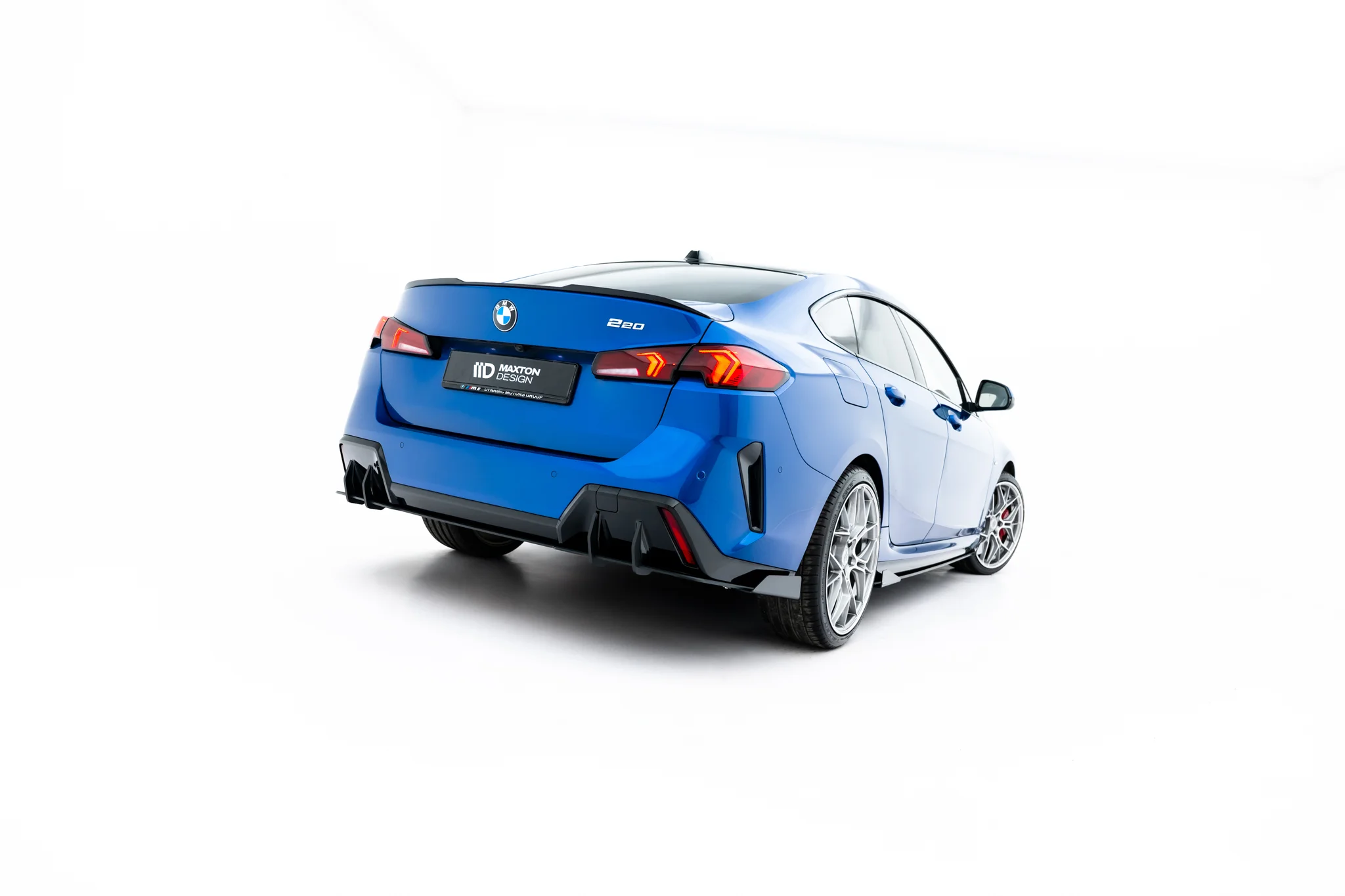 pol_po_Street-Pro-Rear-Diffuser-Flaps-BMW-2-M-Pack-Gran-Coupe-F74-23850_4webp - OPSHOLDERS Rear three-quarter view of a blue BMW 220 with a sporty diffuser and red tail lights in a white studio setting, highlighting the car's wide stance.",