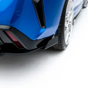Close-up of a blue car's front bumper and left wheel, showing an aggressive black splitter and tire detail.