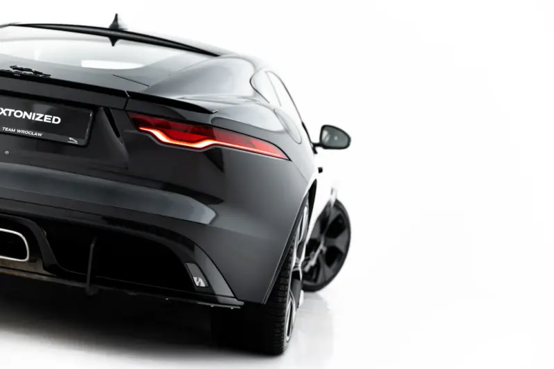 Rear three-quarter view of a sleek black Jaguar sports car showing a red taillight and the license plate reading 'XTONIZED' with 'TEAM WROCLAW' text, against a light background.