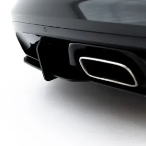 Close-up of a glossy black car bumper and chrome exhaust tip against a light gray background.