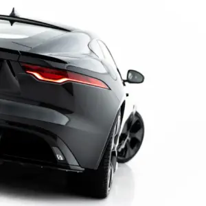 Rear-left view of a dark luxury car showing a red LED taillight and sleek curved body lines on a white background.