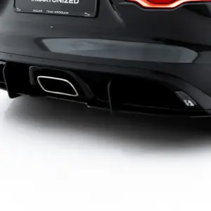 Rear of a dark Jaguar F-Type with a illuminated taillight, quad exhaust and sleek bumper detail.