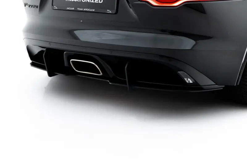 Rear of a dark Jaguar F-Type with a illuminated taillight, quad exhaust and sleek bumper detail.