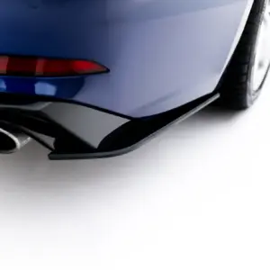 Close-up of the rear corner of a blue car, showing a red taillight, curved bumper, and dual exhaust tips.