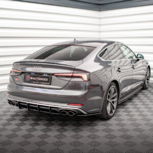 Rear three-quarter view of a gray Audi S5 in a bright studio with white horizontal wall panels behind it.
