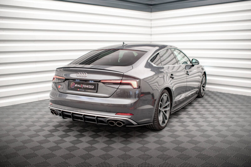 Rear three-quarter view of a gray Audi S5 in a bright studio with white horizontal wall panels behind it.