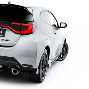 Rear three-quarter view of a silver GR Yaris with red taillights, visible exhaust, and a #MAXTONIZED license plate badge.
