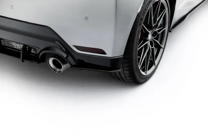 Close-up of a silver car's rear bumper, exhaust pipe, and large alloy wheel.