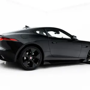 Side view of a sleek black Jaguar sports coupe in a white studio setting, showing the car's profile and red taillight edge.