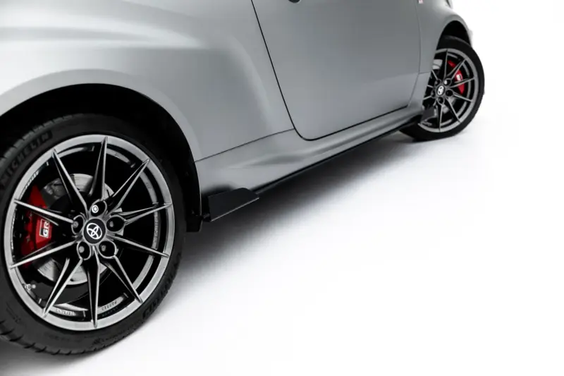 Close-up of a glossy silver sports car body with a large black alloy wheel and red brake caliper visible at the front wheel.