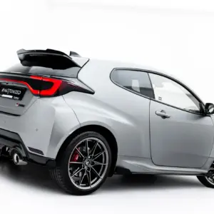 Rear three-quarter view of a silver sports car with the rear hatch spoiler up, prominent red taillights, and large black alloy wheels against a white background.