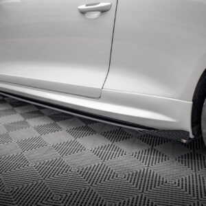 Close-up of a silver car's side panel with door handle and wheel, on a patterned garage floor.