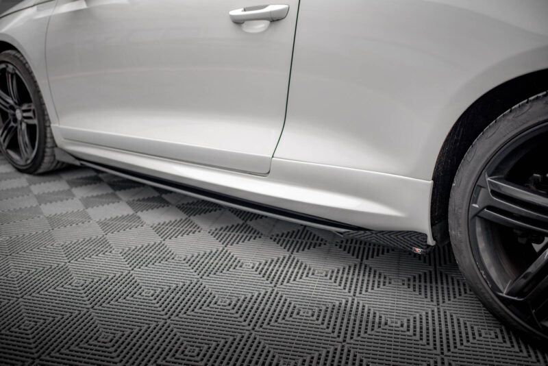 Close-up of a silver car's side panel and front wheel on a diamond-patterned floor.