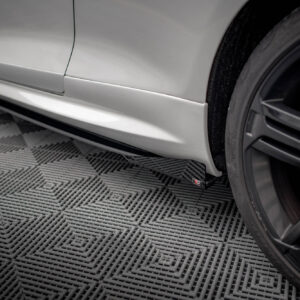 Silver car side panel and lower rocker beneath a wheel, on a textured garage floor; close-up shot showing body panel and mudguard detail.