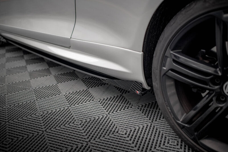 Silver car side panel and lower rocker beneath a wheel, on a textured garage floor; close-up shot showing body panel and mudguard detail.