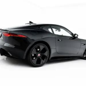 Black Jaguar sports car shown in a studio, rear three-quarter view with red taillights.