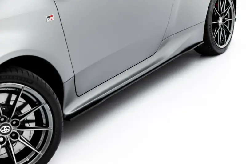 Close-up of a gray sports car side panel showing a GR badge on the door and a large alloy wheel with a low-profile tire.