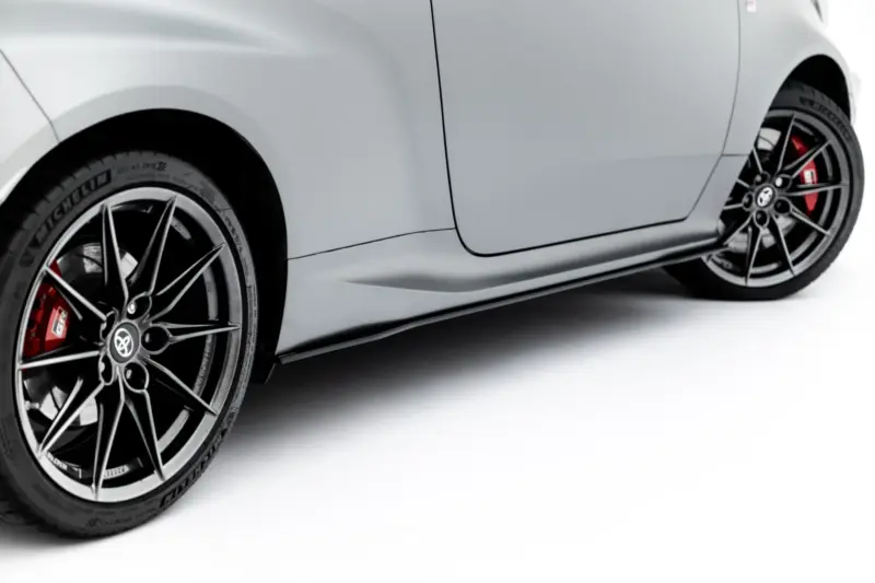 Close-up of a grey car showing front wheel with black alloy rim, red brake caliper, and tire treads visible.