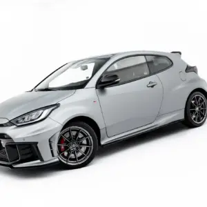 Gray sports car shown from a three-quarter front angle with large black alloy wheels and front splitter, in a studio setting while tilted to the left by the camera angle.