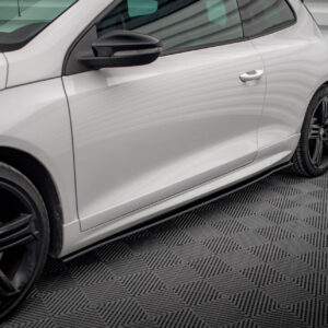 White car side profile with black multi-spoke wheels and visible door handle, photographed indoors on a checkered floor.