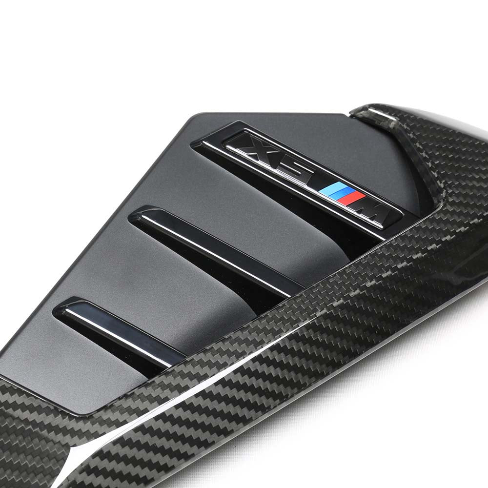 35jpg - OPSHOLDERS Close-up of a carbon fiber car trim piece featuring an M Performance badge with blue, dark blue, and red stripes.