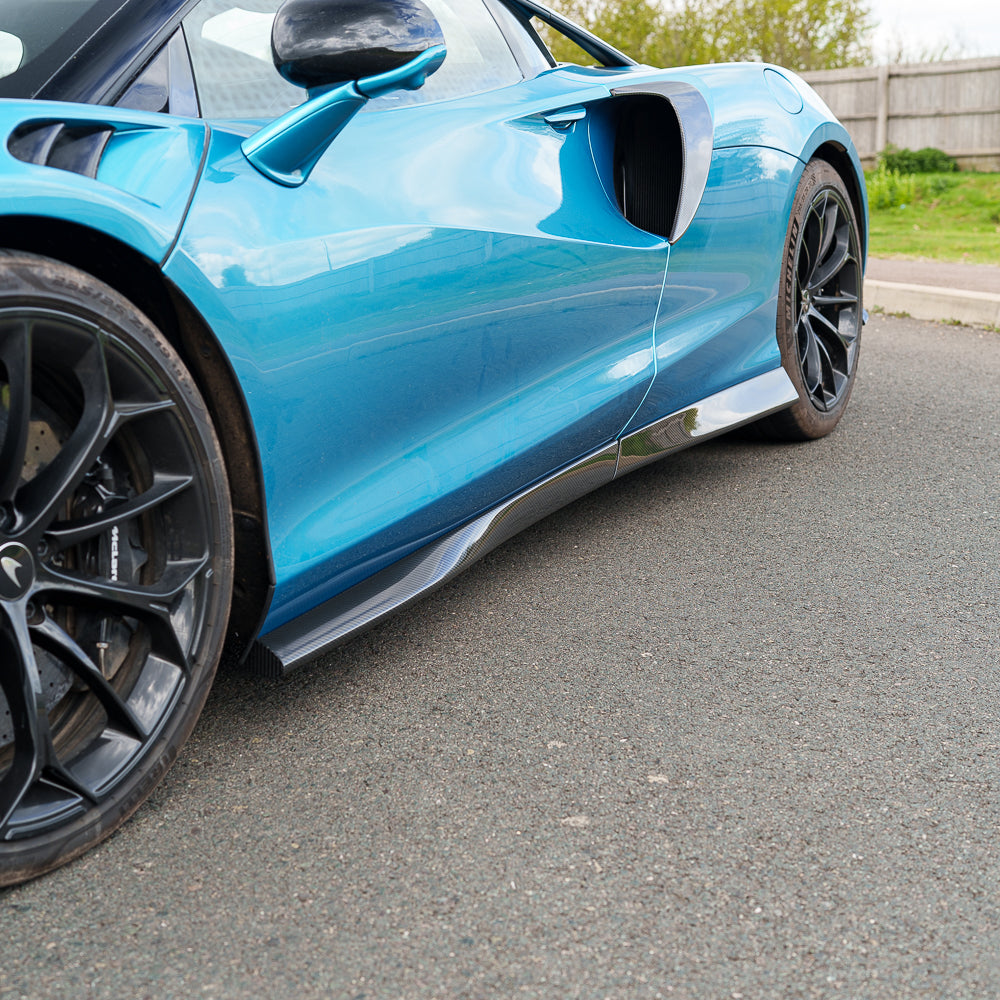 Artura_Web_CT_Carbon_170426_20jpg - OPSHOLDERS Close-up of a blue sports car's side; prominent air intake, carbon fiber side skirt, and large black alloy wheel visible.
