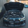 BMW-M2-M3-M4-G87G80G81G82G83-CARBON-FIBRE-SLAM-PANEL-REPLACEMENT-10_a48d3691-acd2-4ca5-89af-c870d00bbeb1jpg - OPSHOLDERS Front view of a BMW with the hood open, showing a high-performance engine bay and carbon fiber accents.