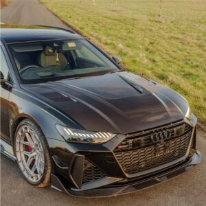 Black Audi RS sport sedan angled from the front-left, parked on a road with a grassy field in the background.