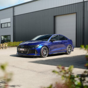 Blue Audi sedan with sporty alloy wheels parked outside a gray industrial building