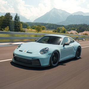 Light blue Porsche 911 GT3 driving fast on a highway with snow-capped mountains in the distance.