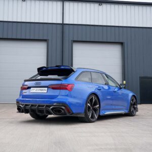 Blue Audi sportback with carbon fiber rear diffuser and quad exhausts parked in front of gray industrial doors, CT CARBON plate visible.