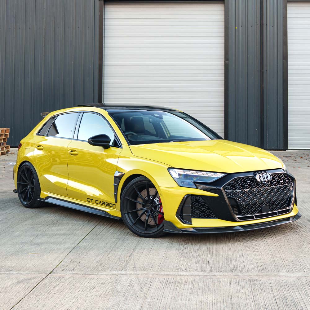 DSC6882jpg - OPSHOLDERS Yellow modified Audi sedan with black large-mesh front grille, carbon front splitter, and black aftermarket wheels parked in front of a dark industrial building