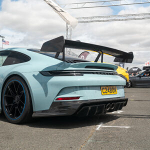 Rear view of a light-blue Porsche with a large carbon rear wing at a car show.