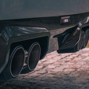 Akrapovic BMW M2 Coupé (G87) OPF/GPF Slip-On Line S-BM/T/39H - OPSHOLDERS Close-up of a dark car's rear with quad exhaust tips and a carbon-fiber diffuser, emphasizing performance styling