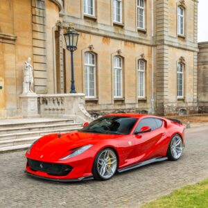 Red Ferrari sports car parked on a cobblestone driveway beside a statue and ornate blue street lamp in front of a beige historic stone building.](https://example)