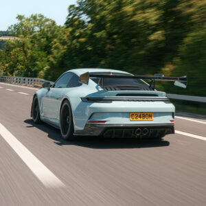 Rear view of a light-blue Porsche-style sports car with a large wing, speeding on a highway.