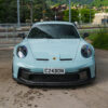 switzerland_porschegt3_1x1_CTCarbon_190626_05jpg - OPSHOLDERS Front view of a light-blue Porsche 911 with a black front splitter and rain droplets on the windshield, license plate C24BON.