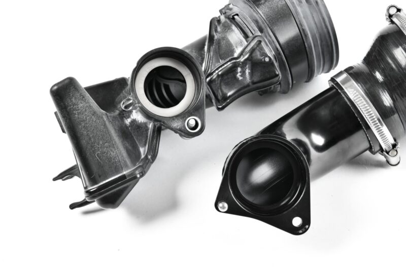 Close-up of an automotive shock absorber/strut assembly with mounting bracket and spring visible, shown in grayscale.