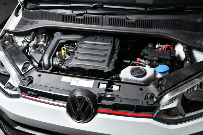 Front view of a VW with the hood open, showing the engine bay including the air intake box and right-side battery.