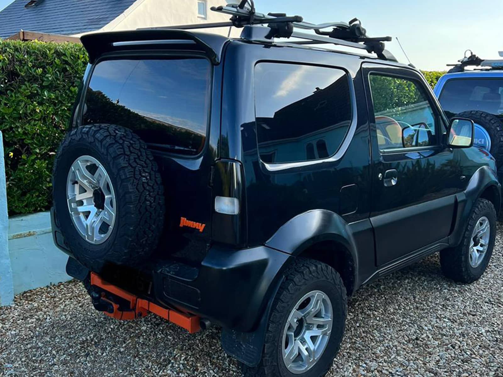 157_1jpg - OPSHOLDERS Rear view of a black compact SUV with a spare tire mounted on the back and a roof rack on top, parked on gravel.