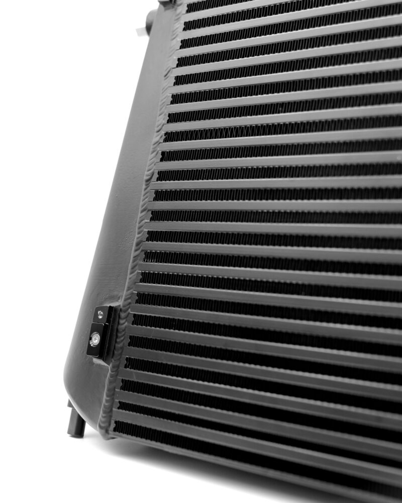 Close-up of a black metal radiator/heat exchanger with horizontal fins, seen in grayscale, with a small cable and mounting bracket at the edge.