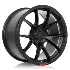 Black alloy car wheel rim with multi-spoke design and red accent at the edge, shown at an angle against a white background, glossy finish.